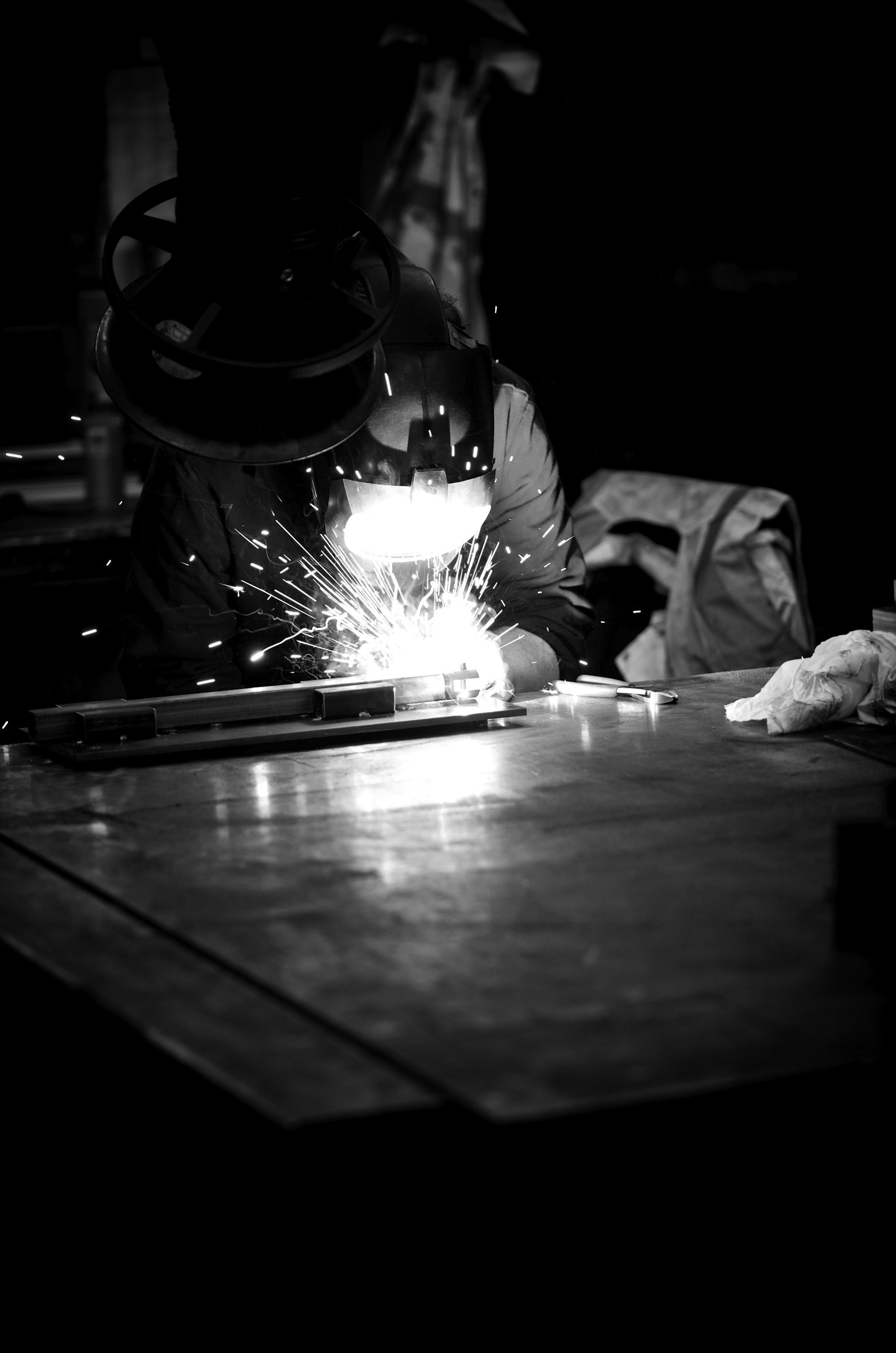 Welder working in darkness with bright sparks flying, dramatic industrial metalwork scene.